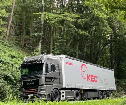 KEC Cargo LKW fährt umweltbewusst durch eine Landstraße im Wald.